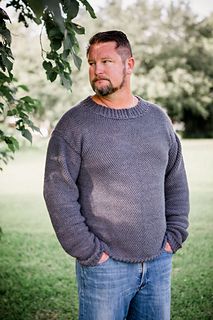 a man standing under a tree wearing a sweater