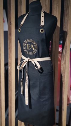 the apron is black and gold with a tan ribbon around it's waist,