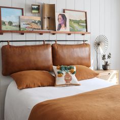 a bed with brown pillows and pictures on the wall above it, along with an orange throw pillow