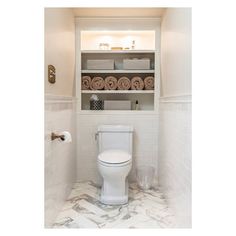 a white toilet sitting inside of a bathroom next to a shelf filled with lots of towels