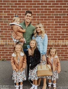 a man and woman with two children standing in front of a brick wall holding a brown purse