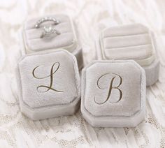 three ring boxes sitting on top of a bed with the initials l, b and c