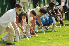 young children playing croquet on the grass with adults watching