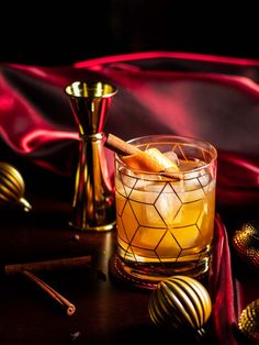 a glass filled with an orange drink next to some gold ornaments and a red satin