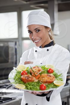 a woman in chef's outfit holding a plate with shrimp and lettuce