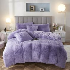 a bed with purple comforter and pillows in a room next to a white chair