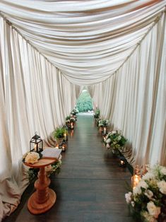 an aisle lined with candles and flowers on either side of the aisle is covered in white drapes