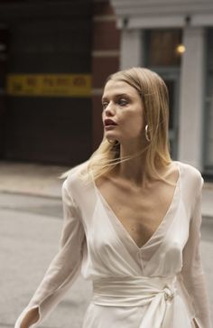 a woman walking down the street wearing a white dress with long sleeves and a tie around her waist