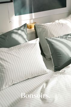 two pillows on a bed with white sheets and green striped pillow cases in front of a window