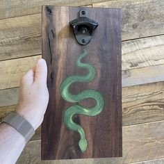 a hand holding a piece of wood with a green snake painted on it