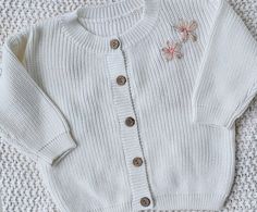 a white knitted sweater with buttons and flowers on the front is laying on a carpet