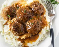 meatballs and gravy over mashed potatoes on a plate with a fork