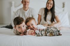 two adults and a child laying on a bed with their arms around the baby's head