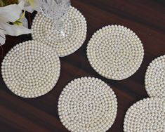 four white beaded coasters sitting on top of a wooden table next to flowers