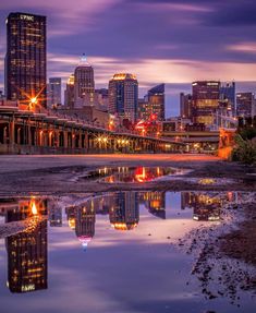 the city skyline is lit up at night with lights reflecting in the water and buildings on either side