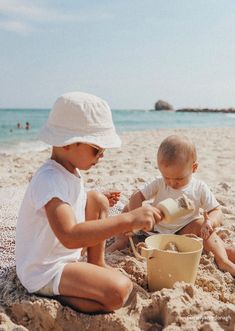 two young children playing in the sand at the beach with buckets and shovels