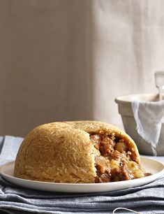 a white plate topped with a piece of bread covered in meat and sauce next to a bowl