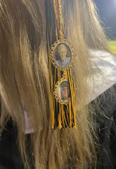 the back of a woman's head with two pictures hanging from her hair and gold tassels