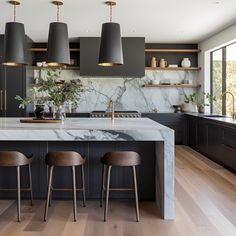 a kitchen with black cabinets and marble counter tops, three stools in front of the island