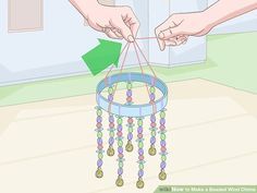 two hands are holding a small blue and green beaded wind chime hanging from the ceiling