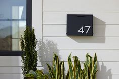 a house number sign mounted to the side of a wall next to two potted plants