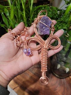 a person holding a wire wrapped cross pendant with amethyst stones on it's side