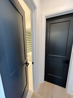 an empty hallway with two black doors and white trim on the walls, leading to another room