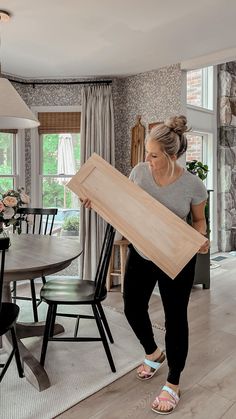 a woman carrying a large piece of wood in her hands while standing next to a dining room table