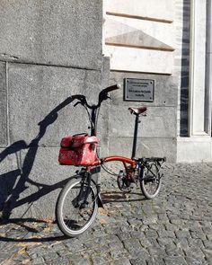 a red bicycle parked next to a gray building on a cobblestone street in front of a stone wall