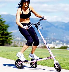 a woman is riding an electric scooter on the sidewalk in front of some grass