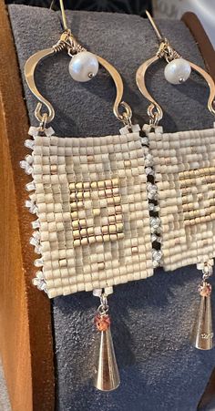 two pairs of earrings with pearls hanging from them on a wooden stand in front of a chair