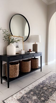 a black console table with baskets under a round mirror on the wall next to a rug