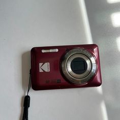 a red digital camera sitting on top of a white table next to a black cord