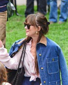 a woman wearing sunglasses and a denim jacket is walking with her hand in the air