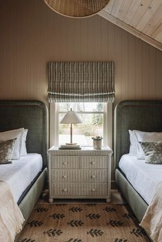 two twin beds in a bedroom next to a window with a lamp on top of it