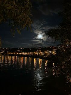 the moon shines brightly in the night sky over a body of water with trees