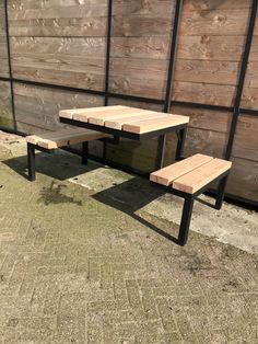 a wooden table and bench sitting in front of a fenced off area with wood planks