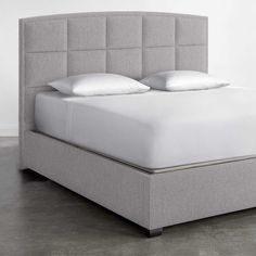 an upholstered bed with white sheets and pillows