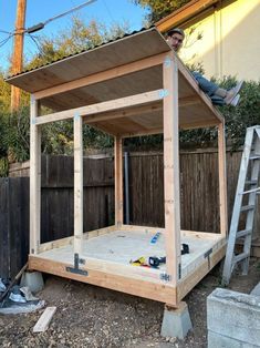 a man sitting on top of a wooden structure in the middle of a yard next to a fence