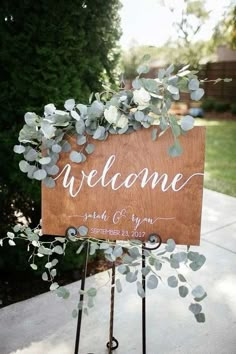 a wooden welcome sign sitting on top of a metal stand next to a tree and bushes