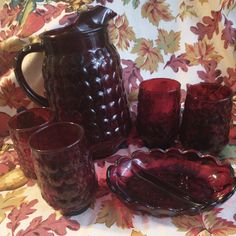 a red pitcher and cups are sitting on a floral tablecloth