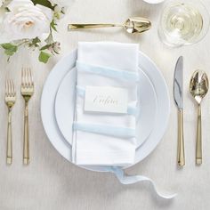 a place setting with silverware, napkins and flowers on a white table cloth