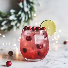 a red drink with cranberries and lime in a glass next to christmas decorations