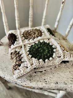 a crocheted chair cushion sitting on top of a wooden table next to a white rocking chair