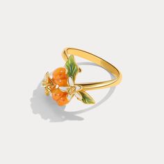 Adorn your hand with the exquisite Golden Plum Flower Ring, a masterpiece that blends nature’s charm with sophisticated craftsmanship. This enchanting ring captures the essence of a flourishing orchard, where golden plums and delicate blossoms come to life in a stunning display of vibrant enamel work. Made from the finest materials, this ring is a true statement piece. The use of enamel adds a glossy finish to the plums and flowers, enhancing their natural beauty and providing a durable, long-la Yellow Gold Enamel Flower Ring Gift, Elegant Enamel Open Ring Jewelry, Exquisite Yellow Gold Flower Ring For Gift, Exquisite Yellow Gold Flower Ring As Gift, Elegant Enamel Rings For Gifts, Enamel Flower Ring For Anniversary, Fine Jewelry Yellow Gold Enamel Ring Gift, Yellow Gold Enamel Ring For Gift, Anniversary Flower Enamel Ring