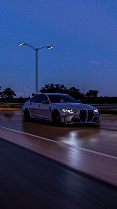 a white sports car driving down the road at night with street lights in the background