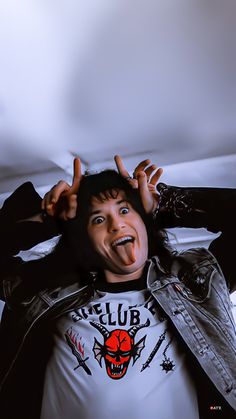 a man with his tongue sticking out and wearing a leather jacket over his shoulders, standing in front of a white background