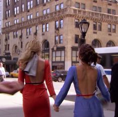 two women in dresses walking down the street with their backs to each other and one holding her hand