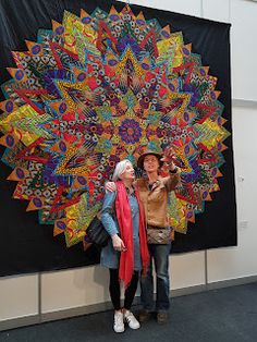 two women are standing in front of a large piece of art that is hanging on the wall