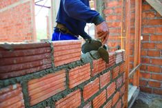 a brick wall being built by a man in blue shirt and black jacket working on it